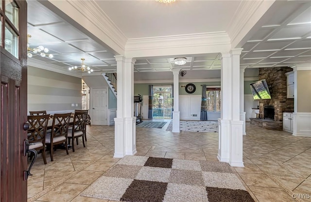 interior space with a fireplace, decorative columns, a notable chandelier, a decorative wall, and ornamental molding