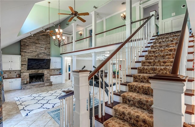 staircase featuring ceiling fan with notable chandelier, high vaulted ceiling, ornate columns, a fireplace, and tile patterned flooring