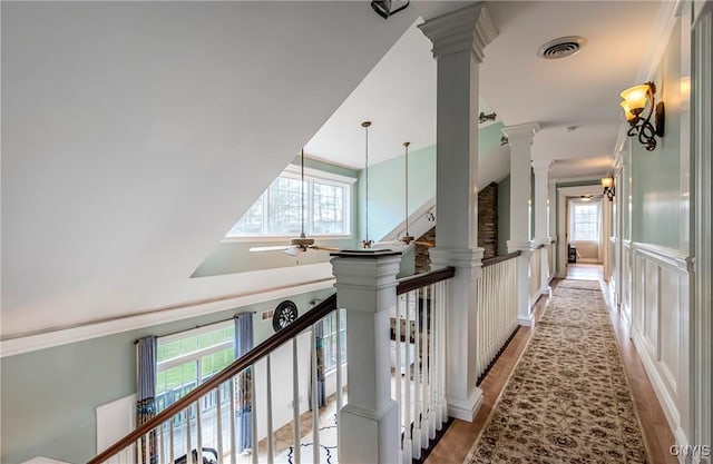 corridor featuring light wood-style flooring, ornate columns, visible vents, and a towering ceiling