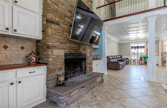 living room featuring light tile patterned floors, a wainscoted wall, decorative columns, a stone fireplace, and ornamental molding