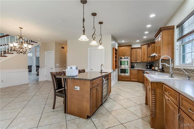kitchen with light tile patterned floors, a sink, brown cabinetry, a kitchen breakfast bar, and appliances with stainless steel finishes