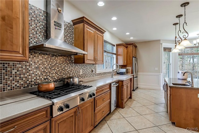 kitchen with wall chimney range hood, appliances with stainless steel finishes, a sink, and a wealth of natural light