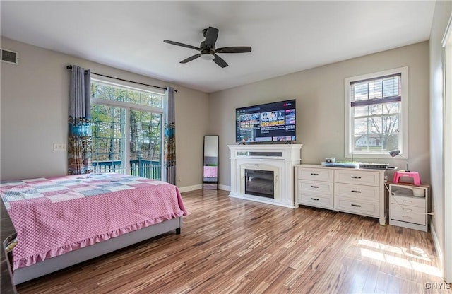 bedroom with visible vents, baseboards, a glass covered fireplace, light wood-style floors, and access to outside