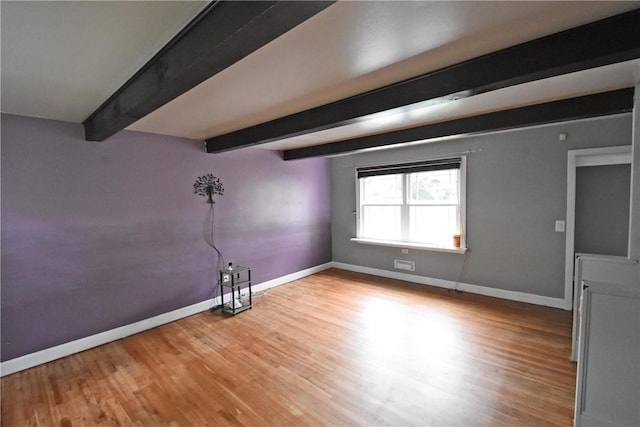 empty room featuring baseboards, beam ceiling, and wood finished floors