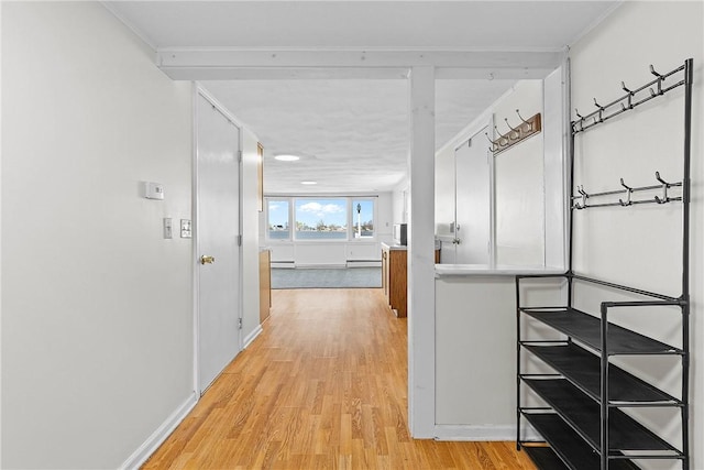 corridor with baseboards, baseboard heating, ornamental molding, and light wood finished floors
