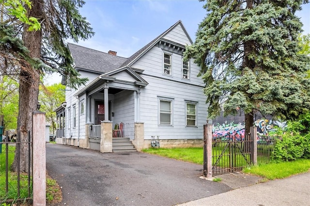 victorian-style house featuring a chimney, driveway, fence, and roof with shingles