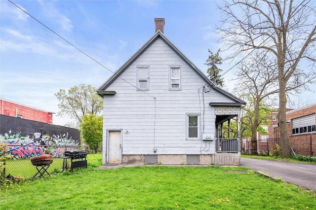 rear view of house featuring fence, a chimney, and a lawn