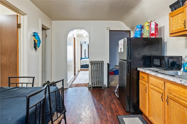 kitchen with radiator, dark wood-type flooring, arched walkways, black appliances, and light countertops