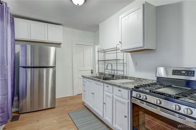 kitchen featuring light stone countertops, light wood-style flooring, a sink, white cabinets, and appliances with stainless steel finishes