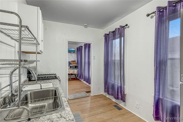 kitchen with visible vents, stainless steel microwave, a sink, wood finished floors, and light countertops