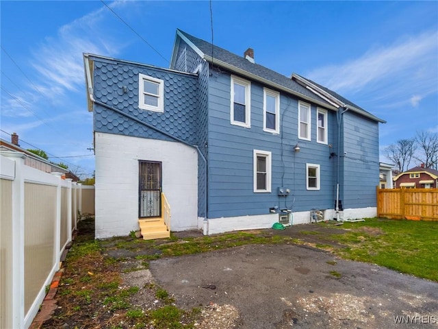 rear view of house with a chimney, entry steps, and a fenced backyard