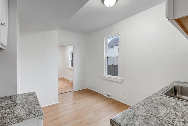 kitchen with a sink, visible vents, light wood finished floors, white cabinetry, and light stone countertops