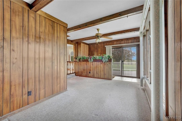 spare room featuring beamed ceiling, wooden walls, light carpet, and ceiling fan