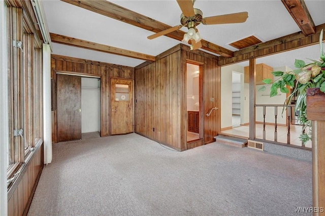 carpeted spare room featuring ceiling fan, wooden walls, visible vents, and beamed ceiling