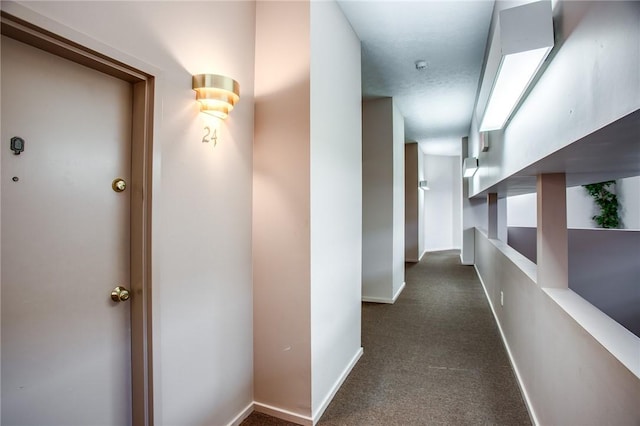 hallway with dark colored carpet and baseboards