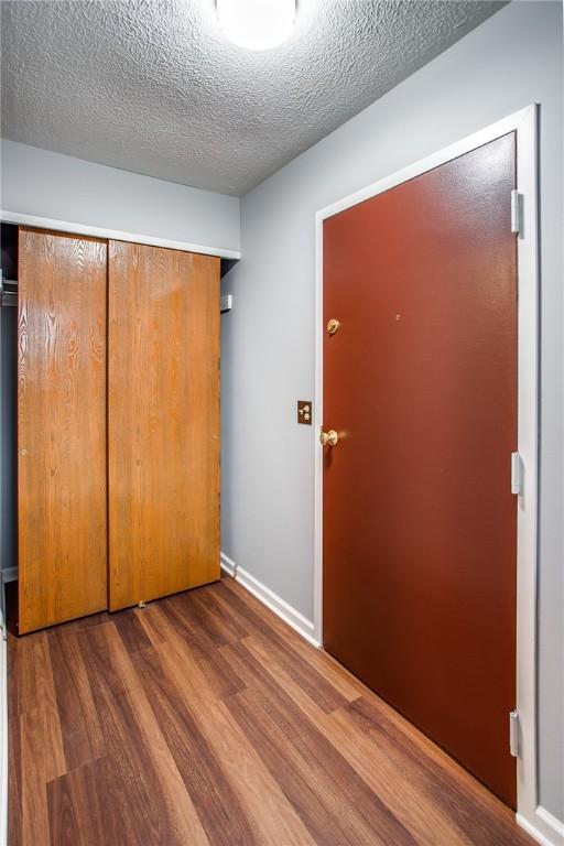 unfurnished bedroom with a textured ceiling, a closet, baseboards, and wood finished floors