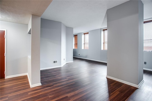 empty room with a textured ceiling, baseboards, dark wood-style floors, and visible vents