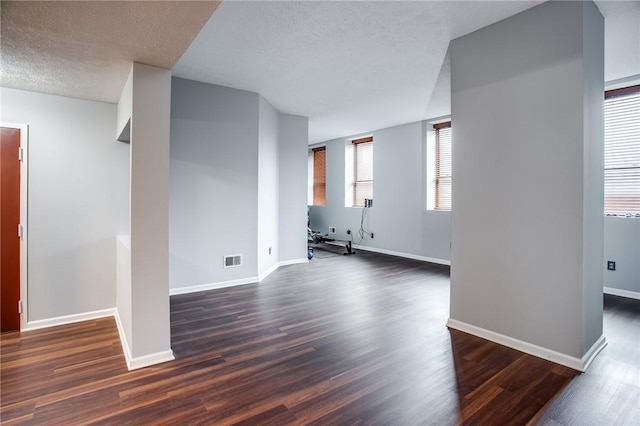 unfurnished living room featuring a textured ceiling, visible vents, baseboards, and dark wood-style floors