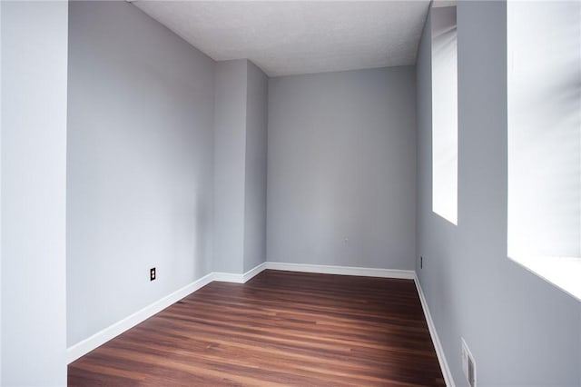 unfurnished room featuring dark wood finished floors, visible vents, baseboards, and a textured ceiling