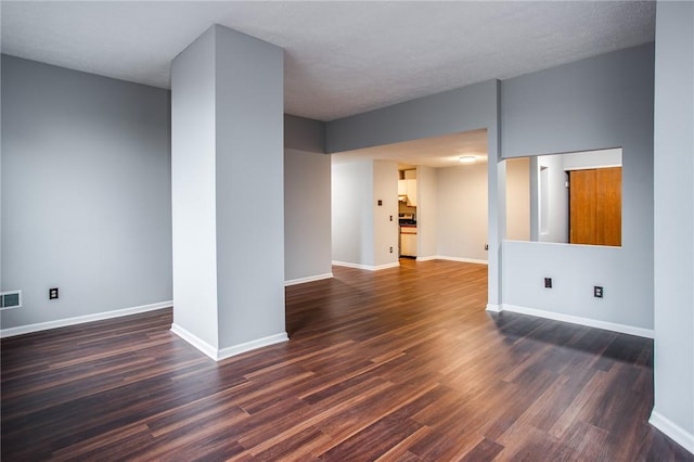 unfurnished living room featuring baseboards, dark wood-type flooring, and visible vents