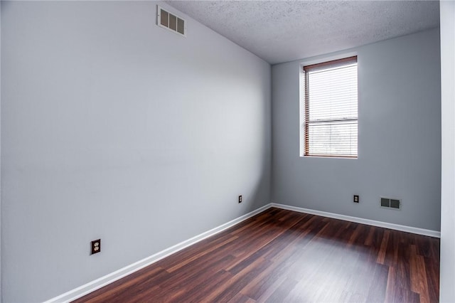 unfurnished room with a textured ceiling, baseboards, dark wood-style floors, and visible vents