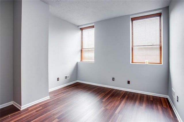 spare room with a textured ceiling, baseboards, dark wood-style floors, and visible vents