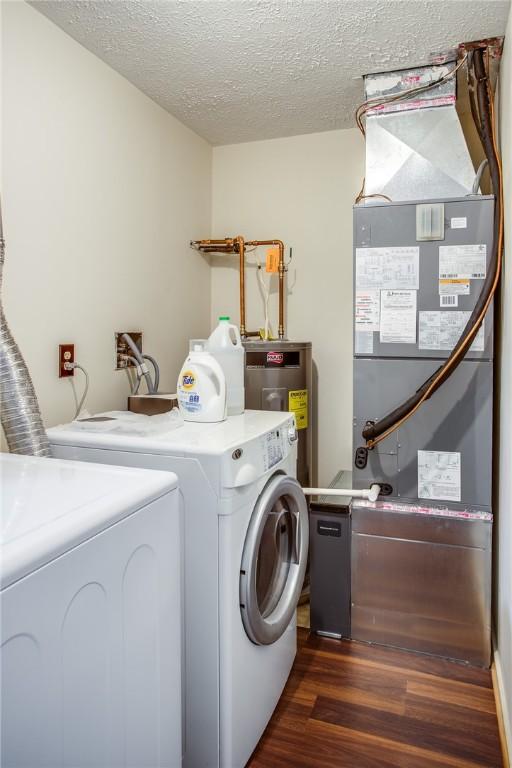 washroom with a textured ceiling, dark wood-style flooring, electric water heater, washing machine and clothes dryer, and laundry area