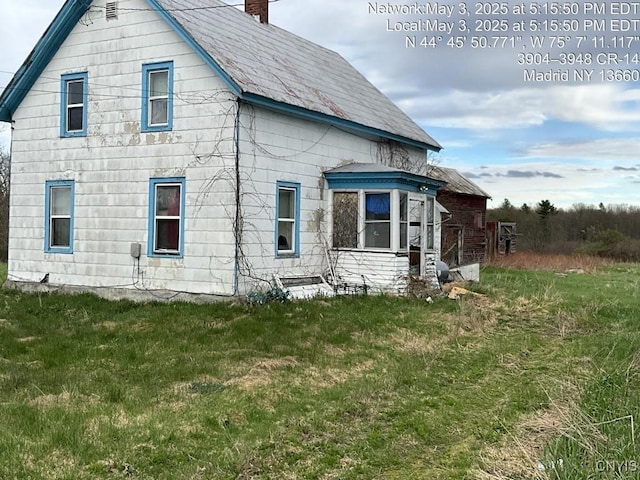 view of side of home with a chimney and a lawn