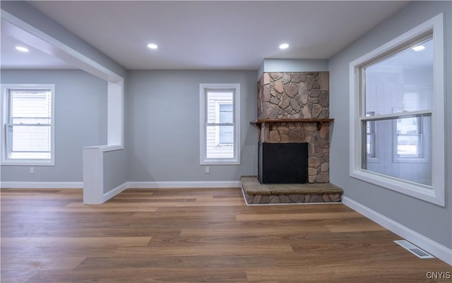 unfurnished living room featuring baseboards, a stone fireplace, visible vents, and wood finished floors