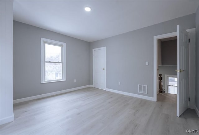 unfurnished bedroom with light wood-type flooring, multiple windows, baseboards, and visible vents