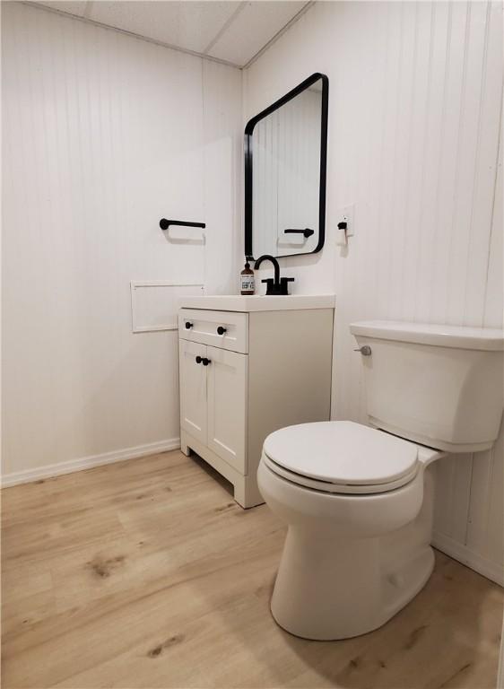 half bath with vanity, toilet, baseboards, and wood finished floors