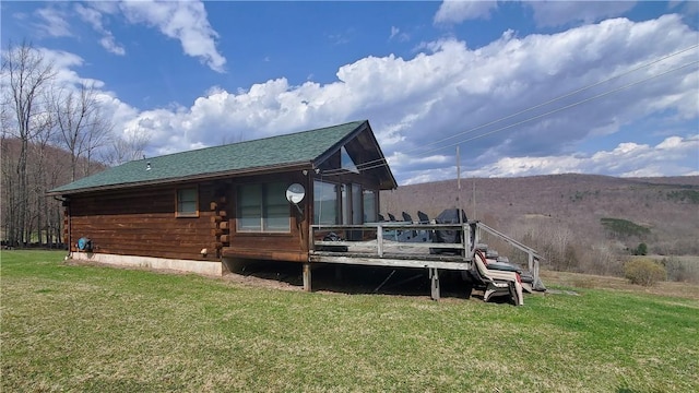 back of house featuring a yard, a deck, roof with shingles, and log exterior