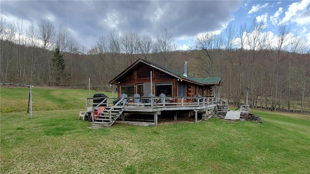 rear view of house with a lawn, a wooden deck, and a view of trees