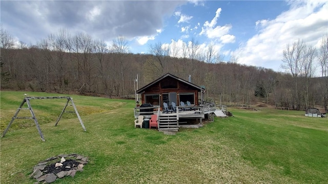 back of property with a wooden deck, a forest view, and a lawn