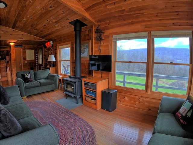 living area featuring a wood stove, light wood-style floors, vaulted ceiling, and wooden walls