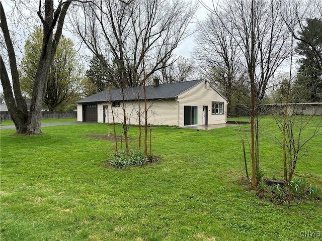 view of yard with fence, an attached garage, and driveway