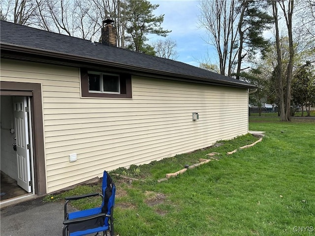 view of side of home with a yard, a chimney, and roof with shingles
