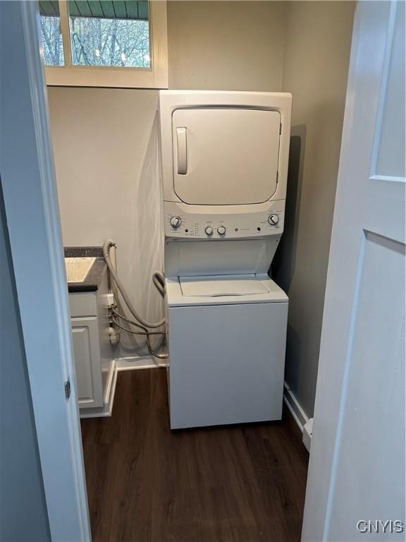 clothes washing area featuring laundry area, stacked washer / drying machine, and dark wood finished floors
