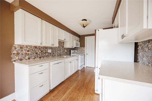 kitchen with white appliances, tasteful backsplash, a sink, light wood-type flooring, and white cabinets
