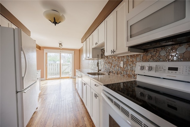 kitchen with white appliances, a sink, tasteful backsplash, light wood-style floors, and white cabinets