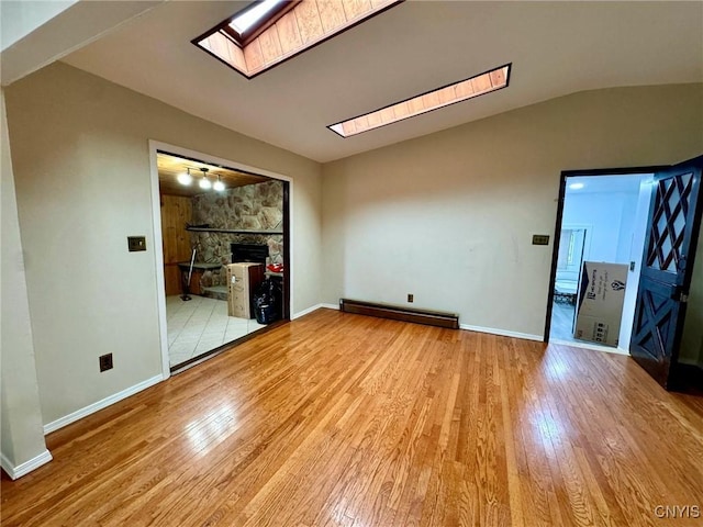 107 Birchwood Ln, Frankfort, NY 13340 - interior space with vaulted ceiling with skylight, baseboard heating, baseboards, a stone fireplace, and light wood-style floors