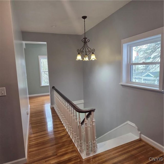staircase with a chandelier, wood finished floors, and baseboards