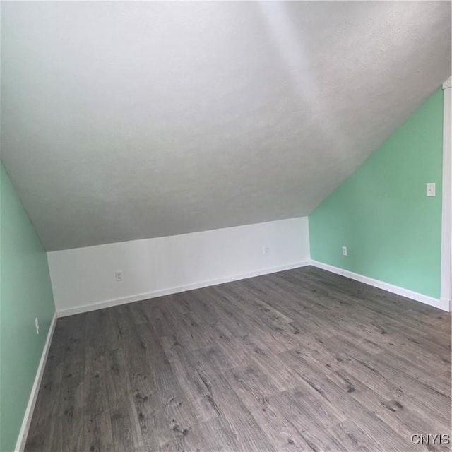 additional living space featuring vaulted ceiling, baseboards, and dark wood-style floors