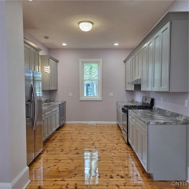 kitchen featuring stainless steel appliances, gray cabinets, baseboards, under cabinet range hood, and light wood-style floors