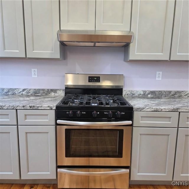 kitchen featuring under cabinet range hood, light stone countertops, and gas range