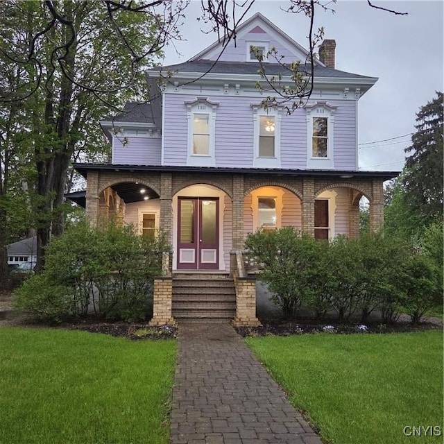italianate-style house with a chimney, a porch, and a front lawn