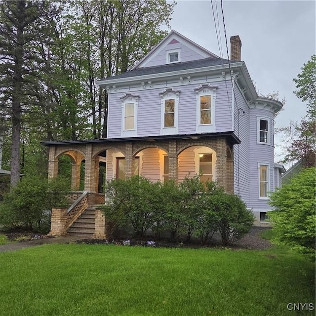 view of front facade featuring covered porch, a chimney, and a front lawn