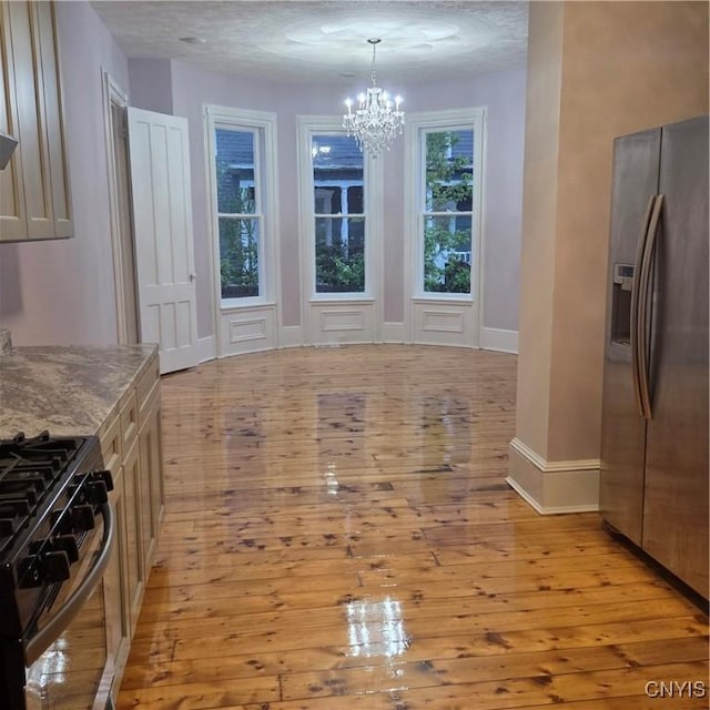 unfurnished dining area featuring an inviting chandelier, light wood-style flooring, a textured ceiling, and baseboards