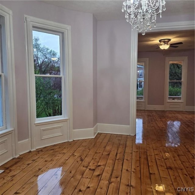 unfurnished dining area with ceiling fan with notable chandelier, wood-type flooring, baseboards, and a healthy amount of sunlight