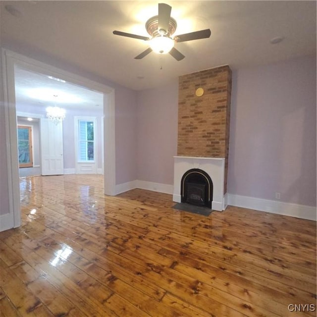 unfurnished living room with baseboards, a fireplace, wood-type flooring, and ceiling fan with notable chandelier